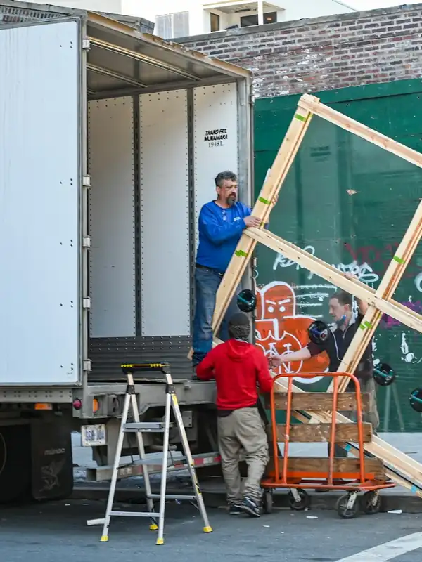 Three workers unloading a large wooden frame from a box truck