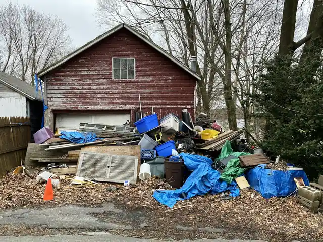 Yard piled with tarps, bins and scrap wood in front of an old red garage