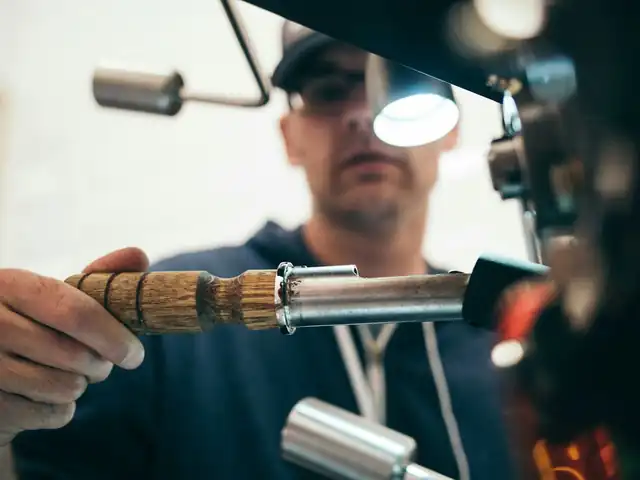Worker in a cap under a work lamp holding a wooden-handled tool