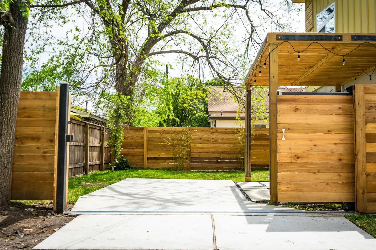 A sunlit wooden fence and patio gate create a serene atmosphere in a backyard, highlighting cleanup challenges.